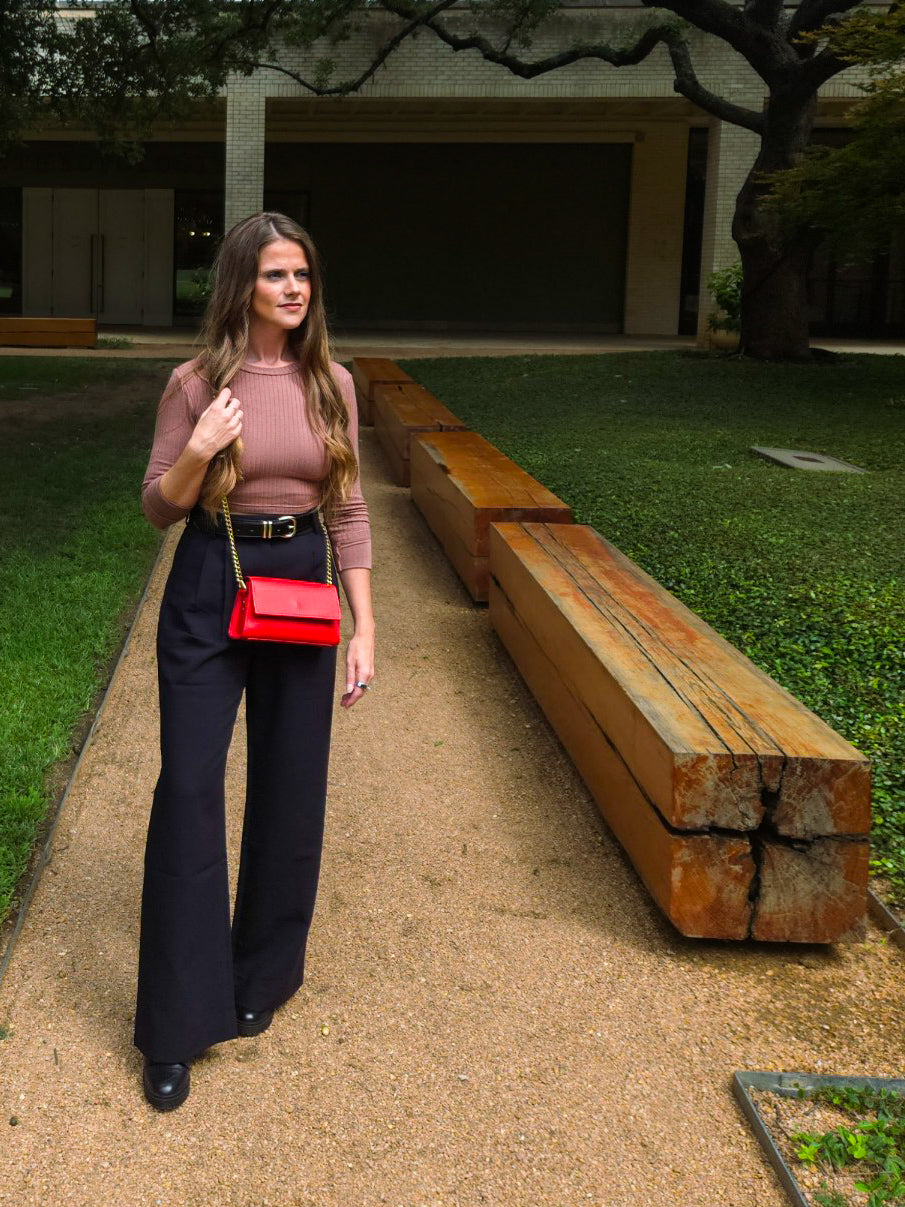 Woman walking outdoors with a red handbag, standing next to wooden planks.